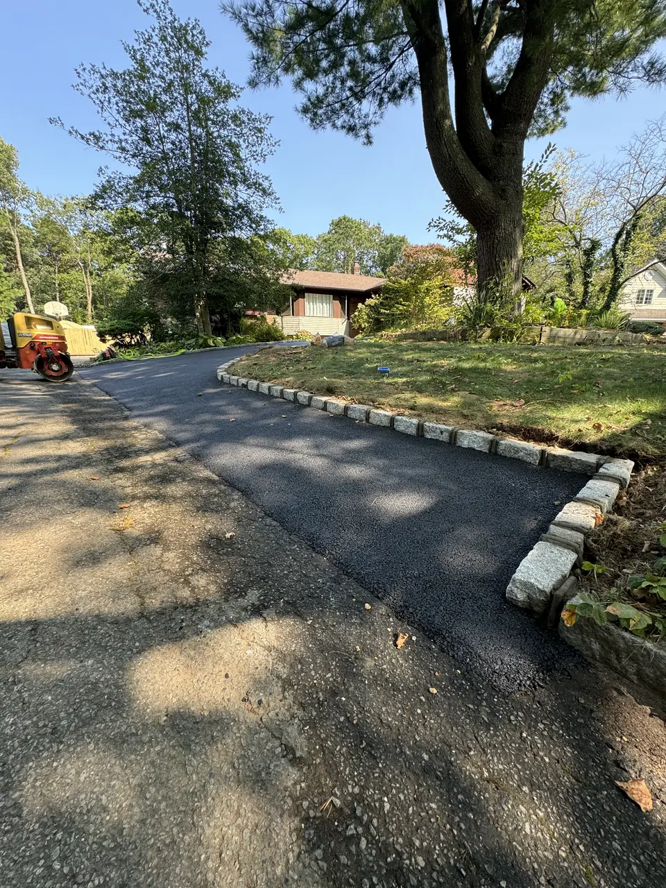 Curving asphalt driveway with block edging through a wooded lot
