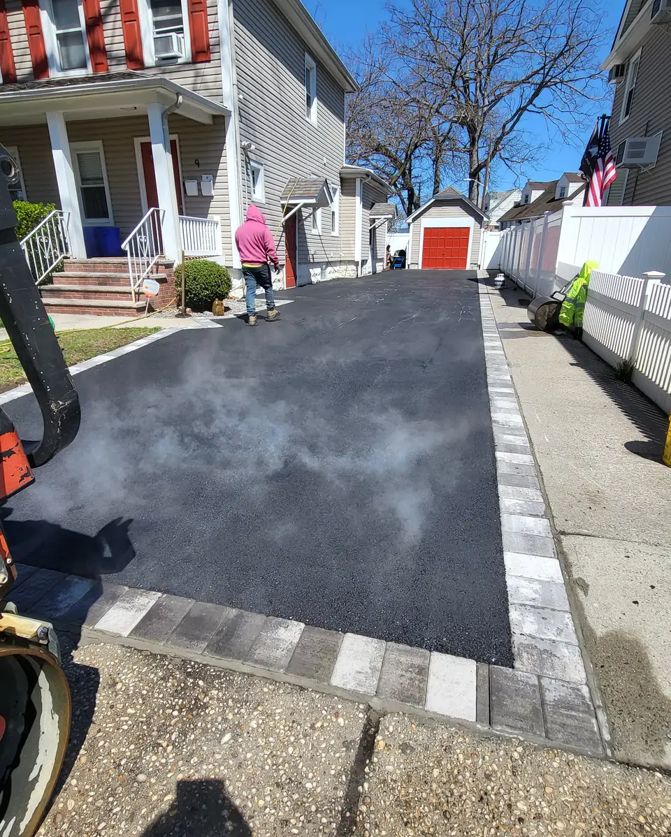 Freshly paved asphalt driveway with a two-tone paver border