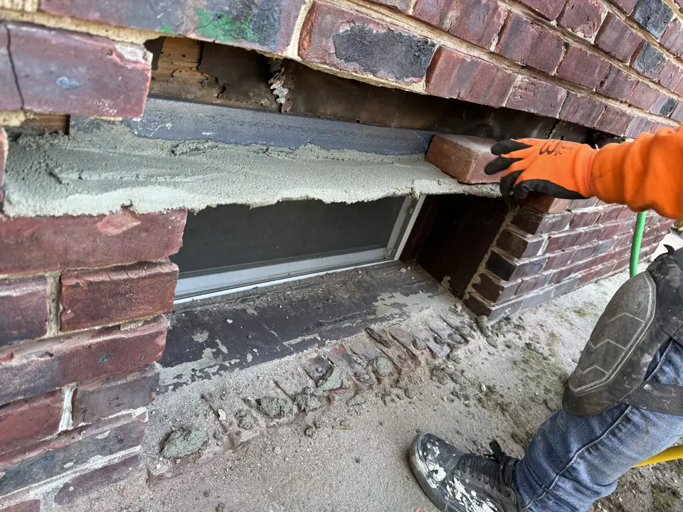 Brick being reset above a basement window opening