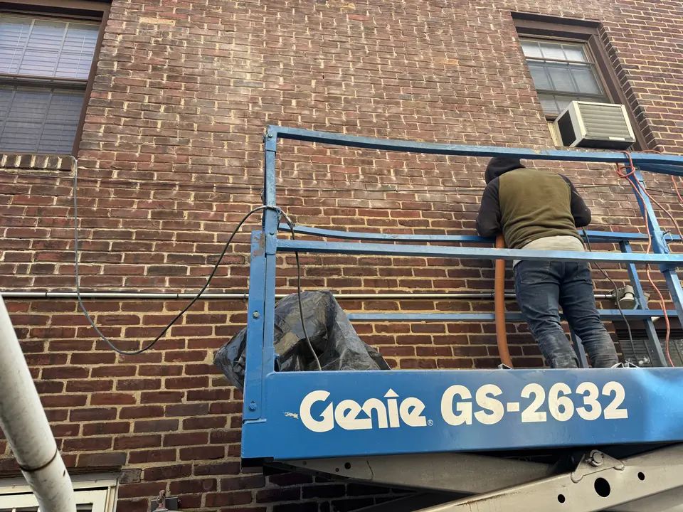 Mason on a lift repointing an upper brick wall